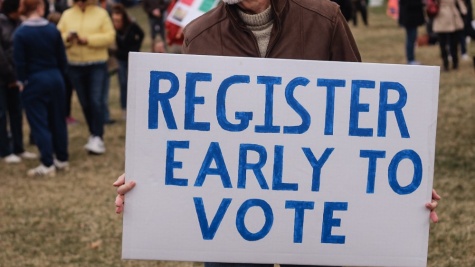 A man holding a sign that says register early to vote