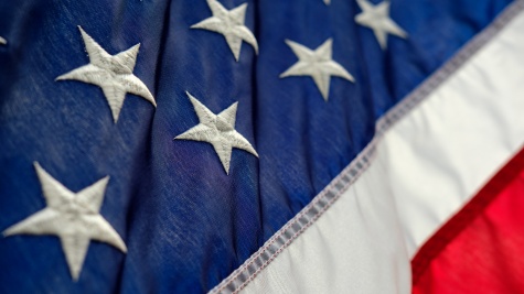 A close-up view of the U.S. flag; we can see about seven stars on the blue background, and two stripes: one white, one red.