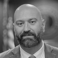 A black and white photo of Jared, who is bald with a beard, in a grey suit and tie.