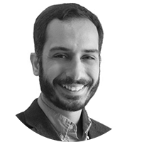 A black and white photo of a bearded man in a collared shirt and jacket, smiling at the camera.