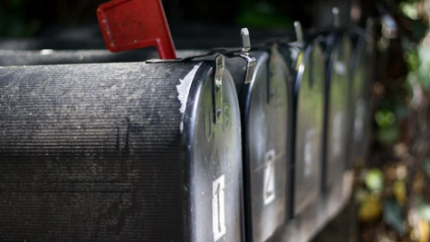 A side view of a line of black mailboxes. The mailbox in the foreground has a red flag raised.