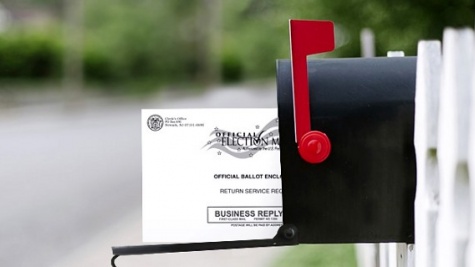A mail ballot hanging out of a black mailbox with a red flag raised