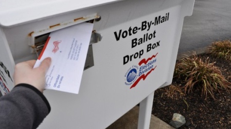 Image of a person placing their absentee ballot in a vote-by-mail ballot drop box.