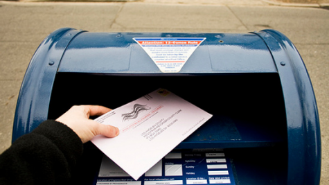 Photograph of person dropping absentee ballot in a USPS drop box.
