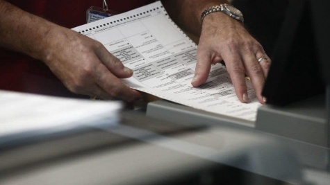 White masculine hands hold a ballot over a table