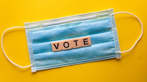 A picture of a surgical mask with a yellow background and the mask says vote on it