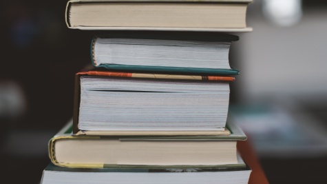 A stack of hardcover books rests on a table, the spines facing to the left.