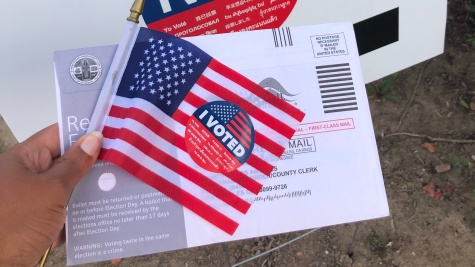 Someone holds an American flag with an "I voted" sticker on it, and an envelope for an absentee ballot