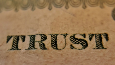 A close up of the word TRUST written in gothic serif font on a brown piece of paper.