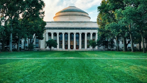 The Great Dome of MIT on a sunny late afternoon in summer. The sky is blue with some fluffy clouds, and a green lawn stretches between the camera and the dome building.