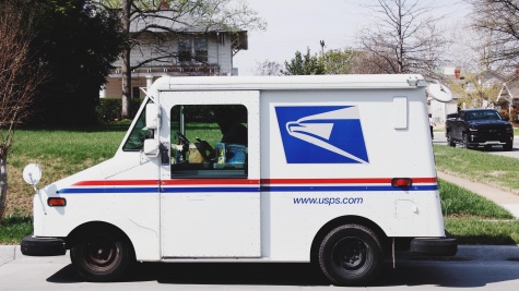 A white USPS truck is stopped at the curb in a suburban neighborhood.