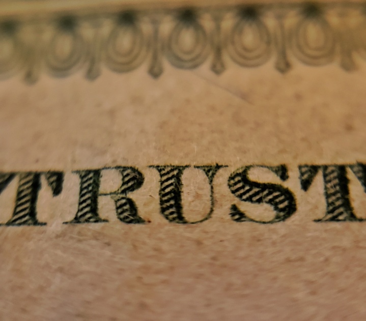 A close up of the word TRUST written in gothic serif font on a brown piece of paper.