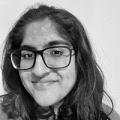 A close-up shot of a young brown woman with glasses and long, slightly wavy hair smiling at the camera.