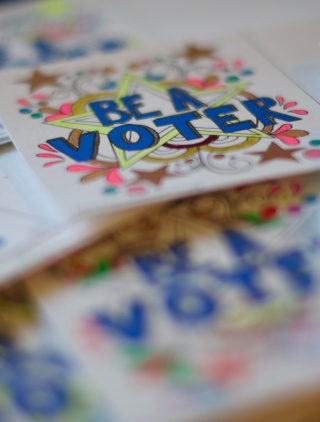 A close-up shot of a pile of brightly colored "Be a Voter" stickers.