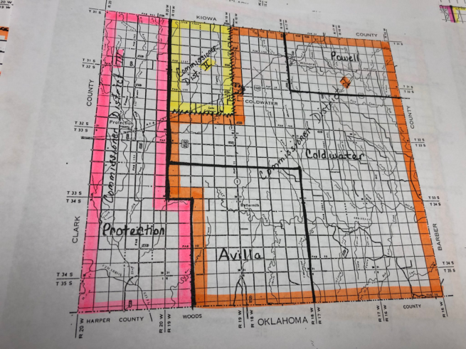 An old map of Comanche County, KS commission districts. The map low-quality, geographic map, with the 3 districts cut in perpendicular lines, outlined in orange, pink, and yellow highlighter. The counties and commission districts are handwritten in pen over the map.